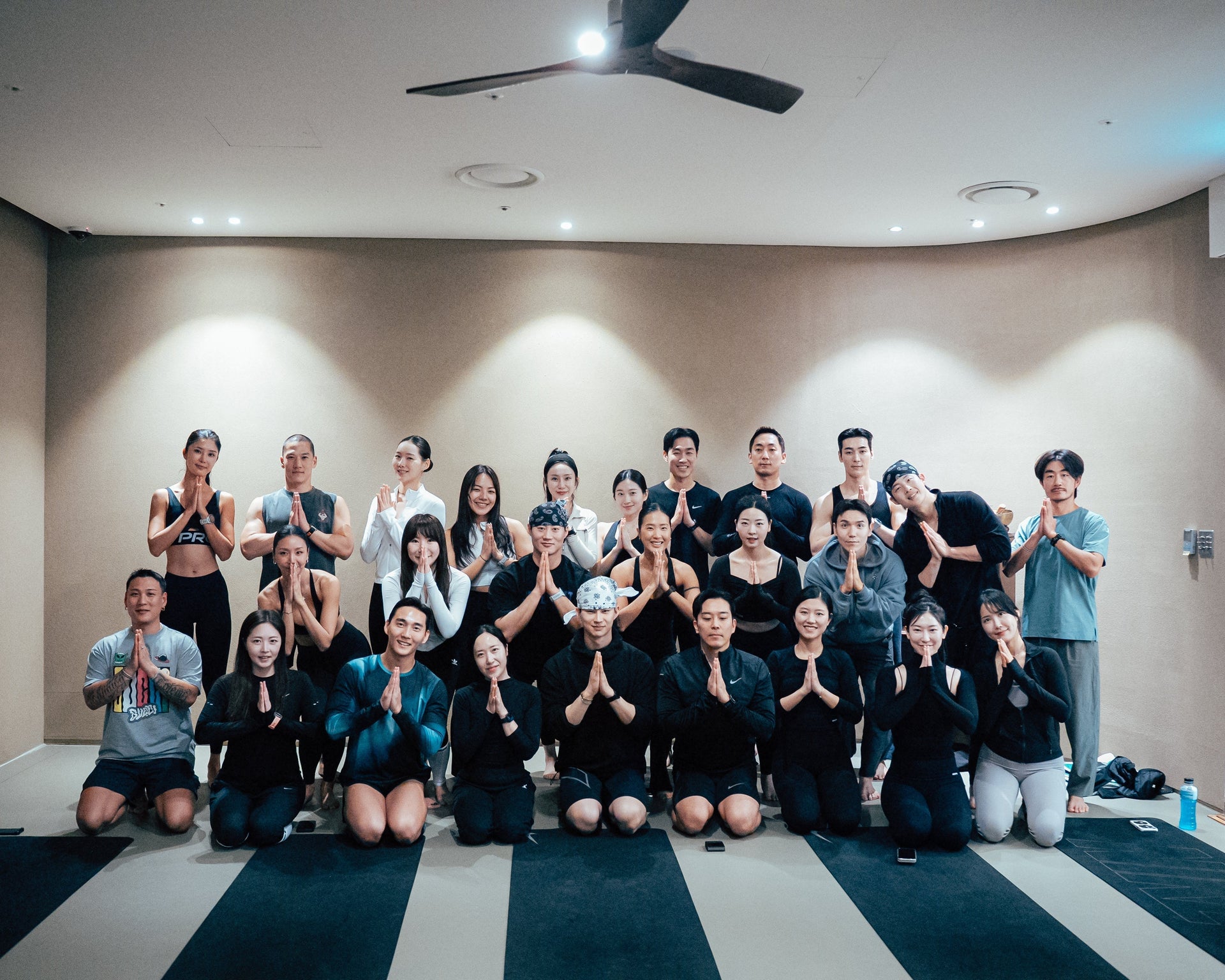 Group of people posing indoors with hands pressed together in a greeting gesture