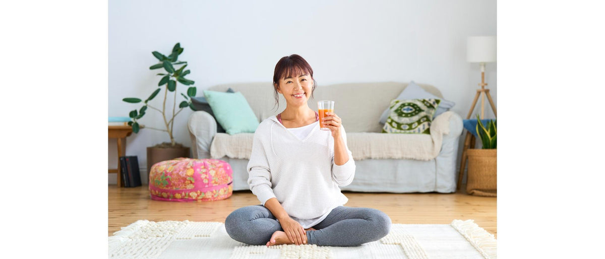Person sitting cross-legged on the floor in a living room, holding a glass of juice