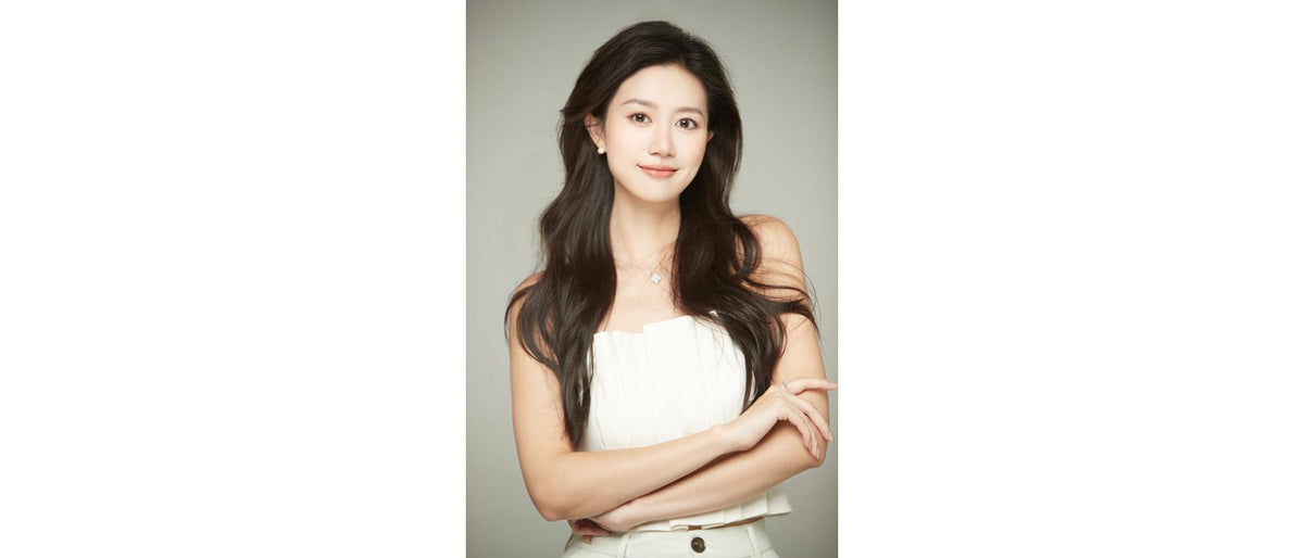 Person with long hair standing with arms crossed against a plain background