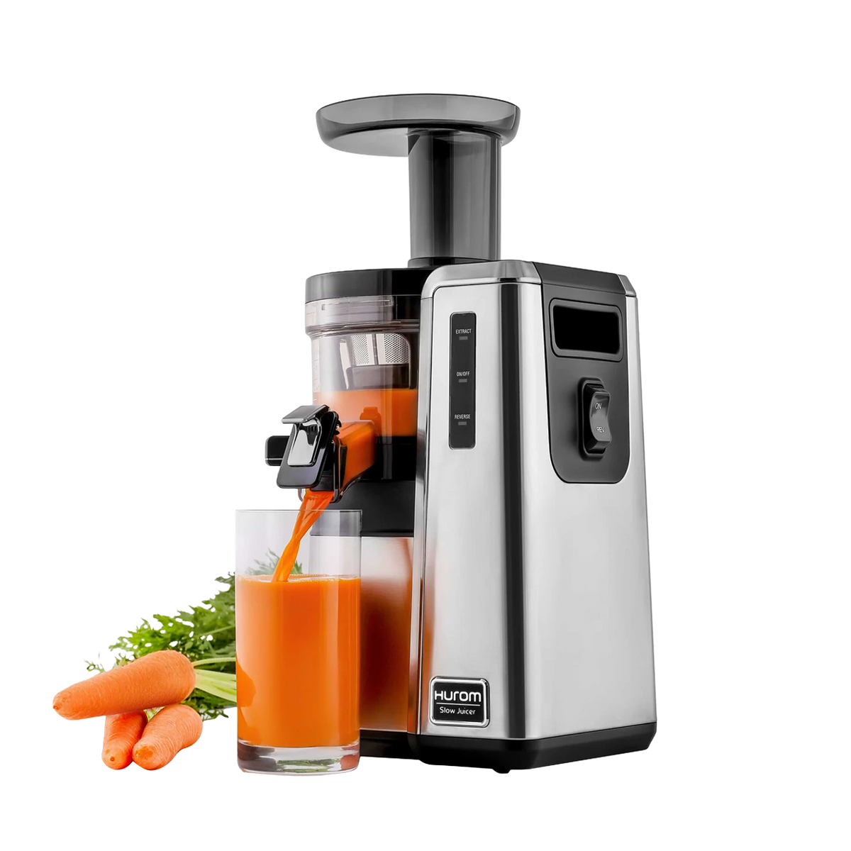 A Hurom slow masticating juicer in stainless steel and black, shown with orange juice pouring into a glass and carrots and greens beside it on a white background.